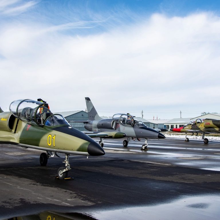Photo of three L-39 Aircraft parked on a tarmac with snow in the background.