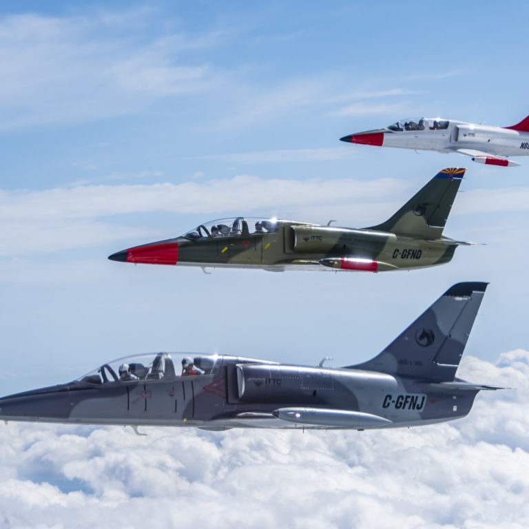 Photo of three L-39 Aircraft flying in formation with clouds and blue sky.