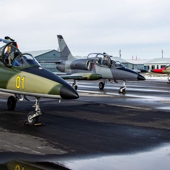 Photo of three L-39 jet aircraft with snow in the background sitting on the tarmac.