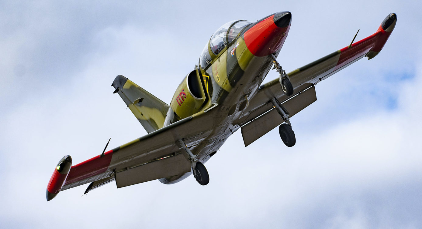 Photo of green camoflauge L-39 jet aircraft flying with wheels down.