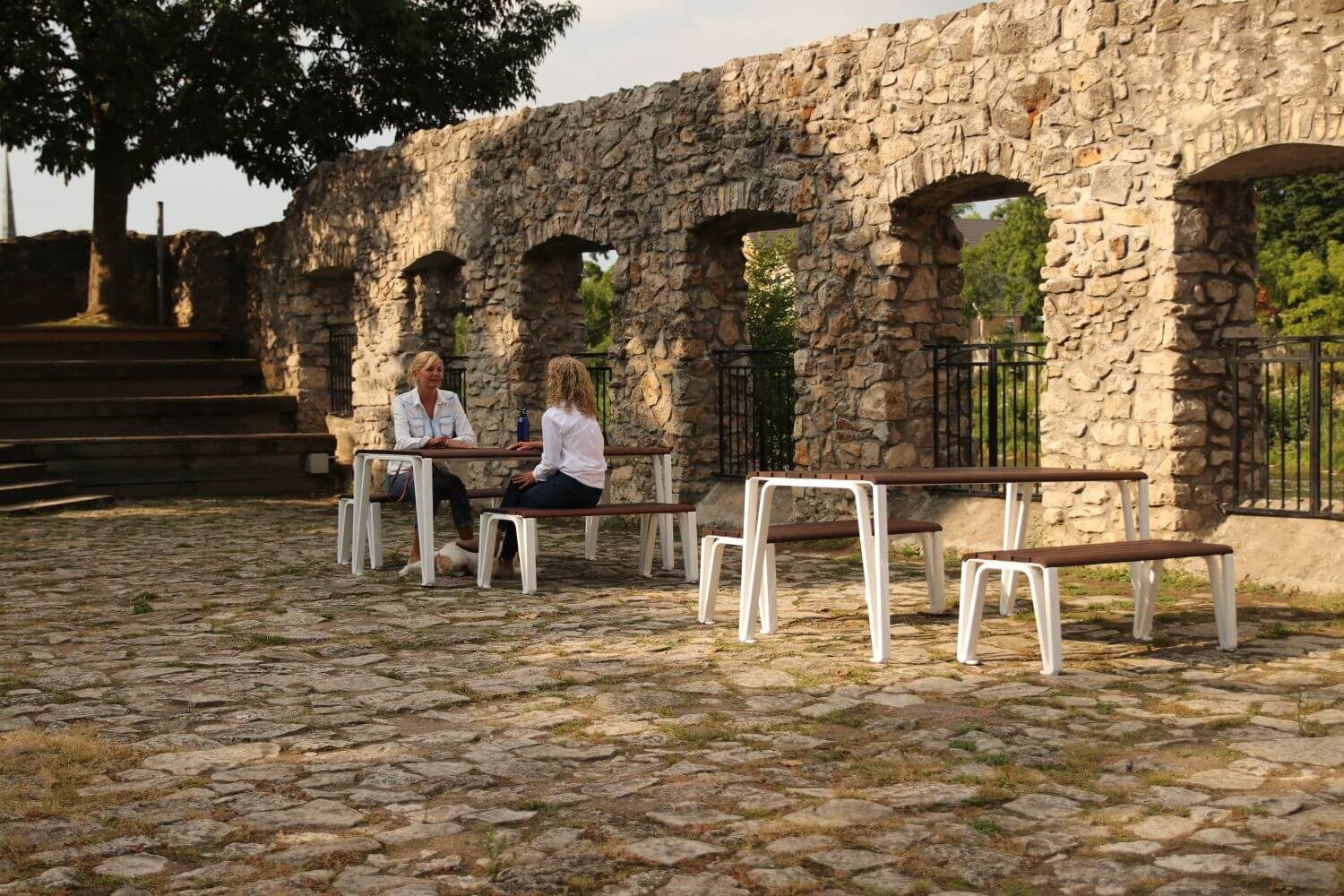 white legged tables with wood top. In the background two women are sitting at a table