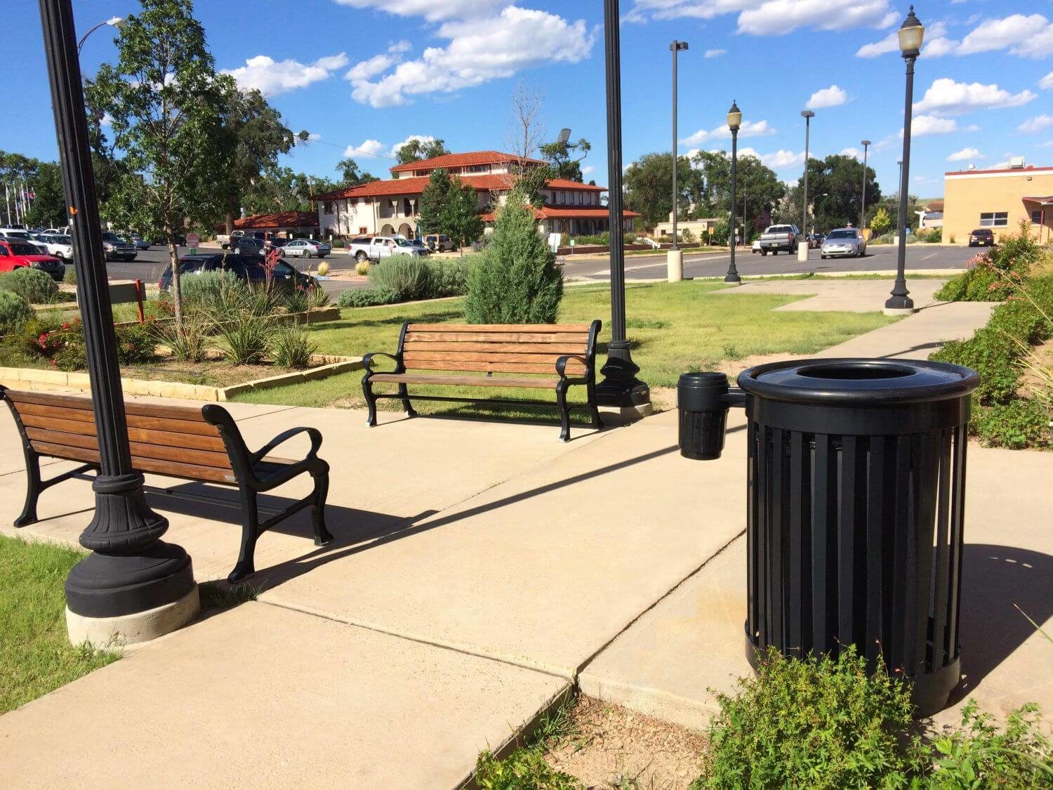 Black trash can near wooden benches and walking paths.