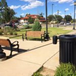 Black trash can near wooden benches and walking paths.