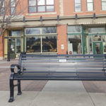 Black Metal Bench with Horizontal Slats Near Commercial Shops