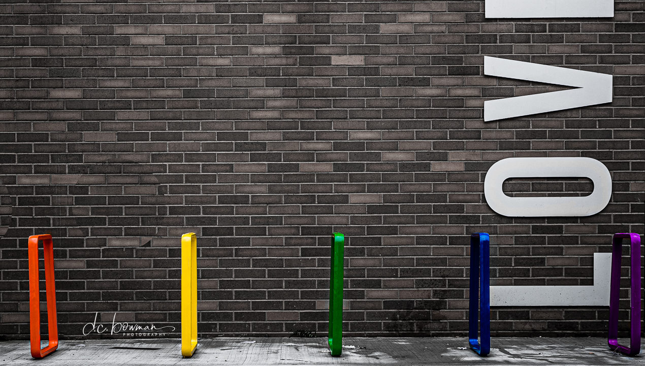 Bright Coloured Bike Racks near brick wall that says 