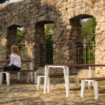 Two women sitting at ICONIC table and benches outside near a stone wall
