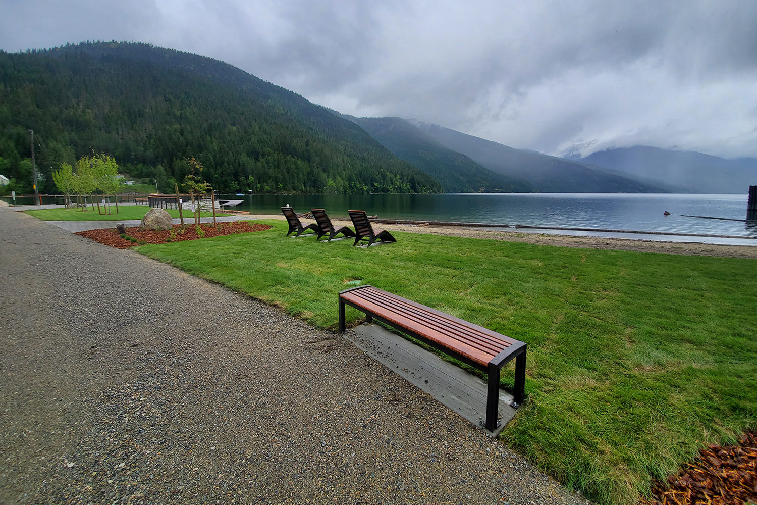Three lounge chairs and a wood bench overlook a calm lake