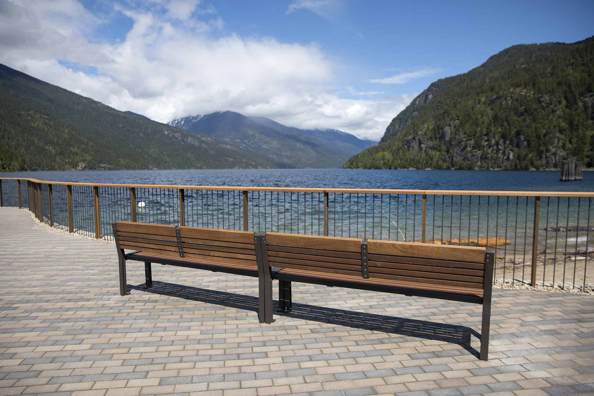 Two wood benches on a paved breakwater overlooking a lake and mountains