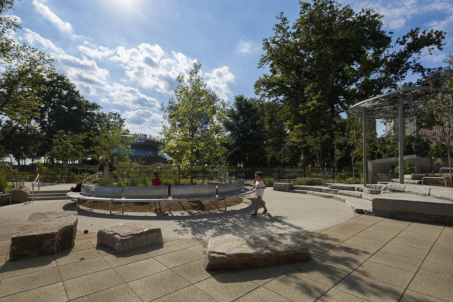 Two children walk by metal benches at the Battery Playscape