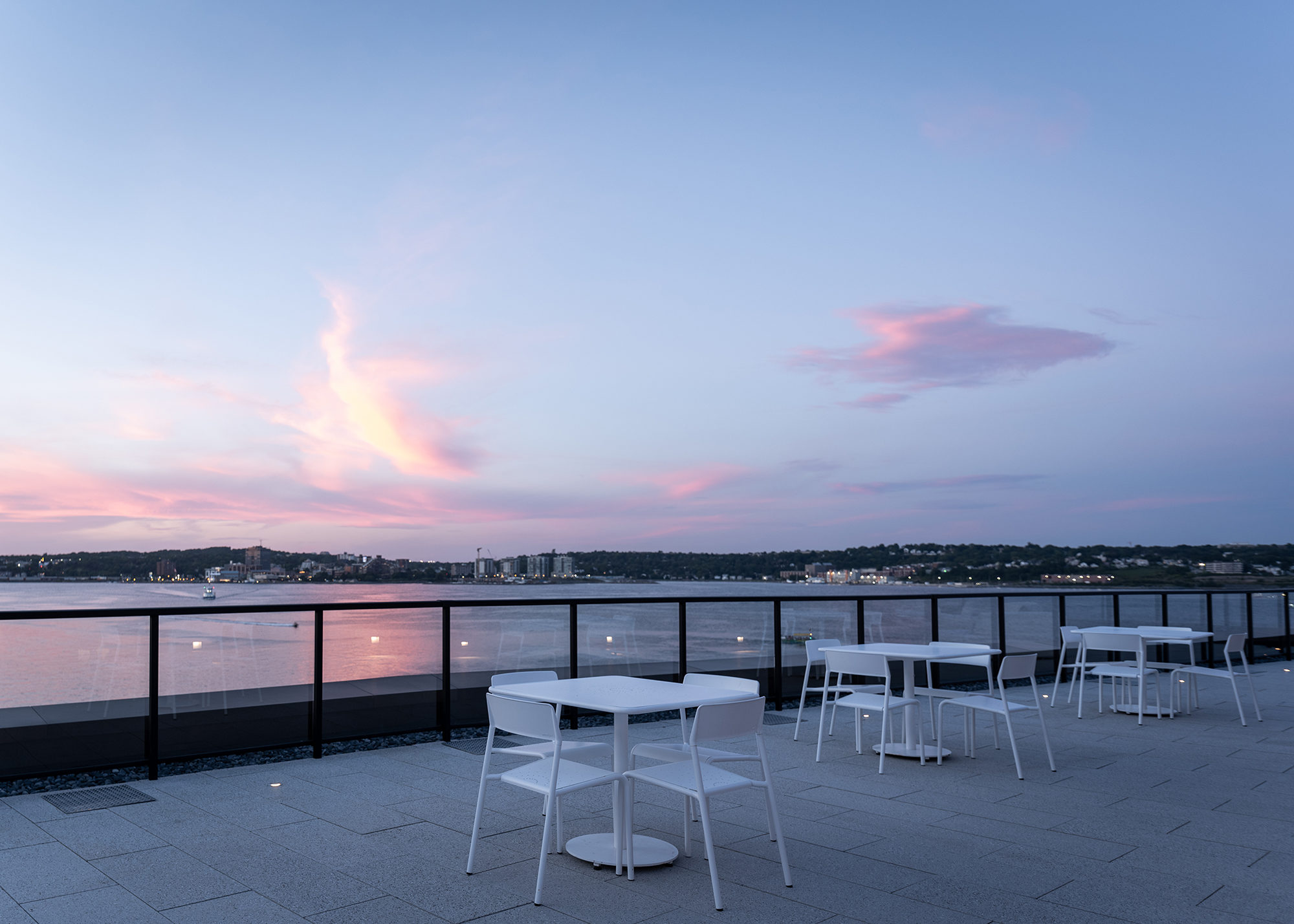 Evening view of white Foro tables and chairs overlooking the ocean from the Stewart McKelvey rooftop terrace