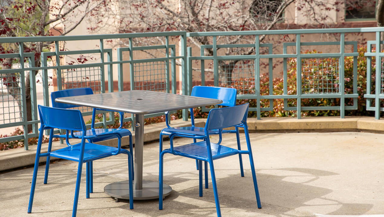 Square Foro Table and Seating, blue and gunmetal powdercoat on a patio with fence in background
