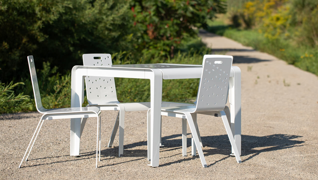 ALUM dining table with chairs powdercoated white with Fusion pattern on pathway with greenery in background