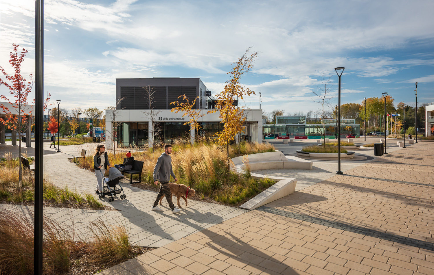 agora-ogden-backed-and-backless-650-trash A child sits on a Maglin Ogden Bench while a woman walks by with a stroller and a man walks a poodle-type dog on a pathway in Agora Plaza, Gatineau, QC. There is plentiful outdoor seating for comfortable use outdoors.