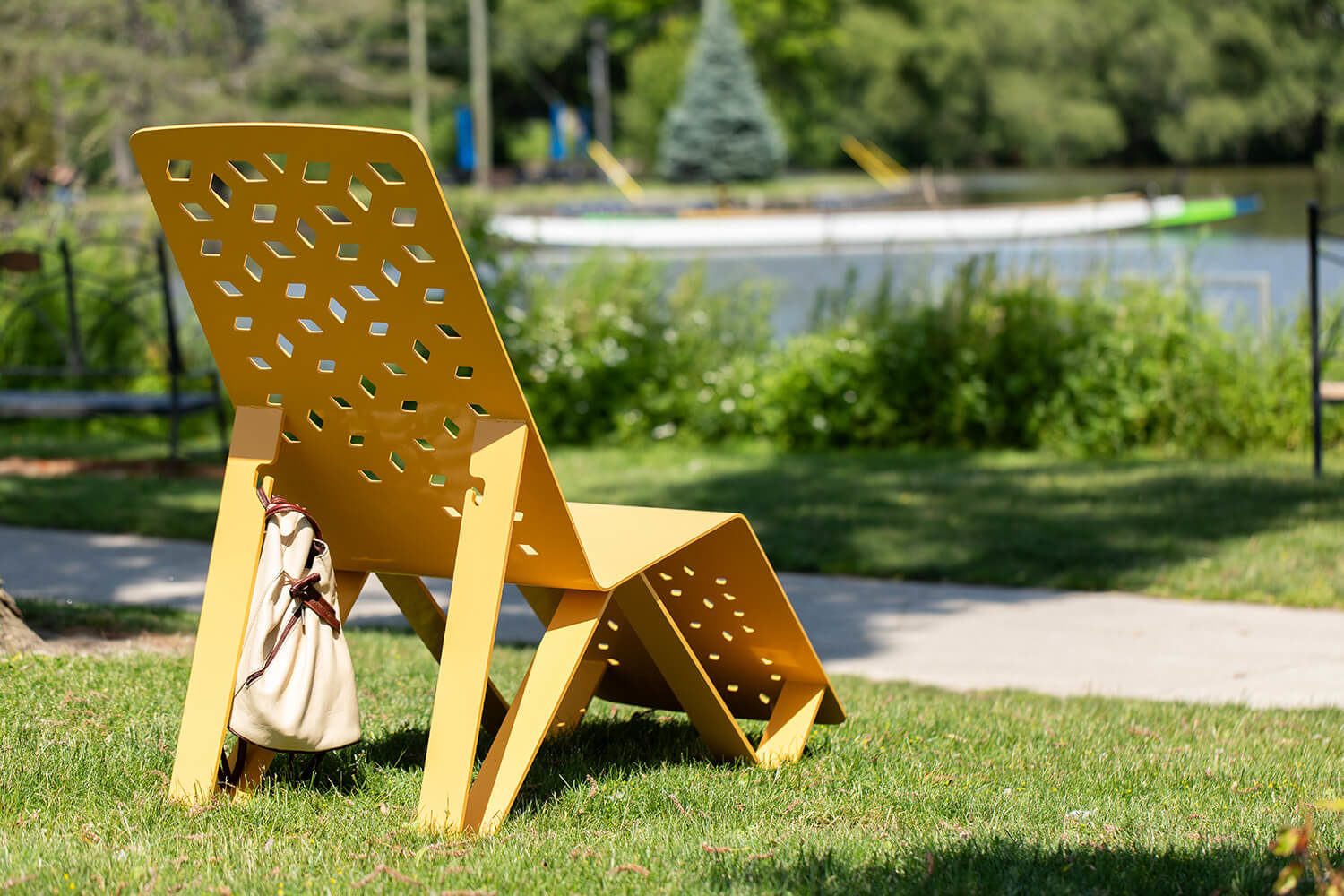 Yellow ALUM chaise lounge with bag attached facing water on grass