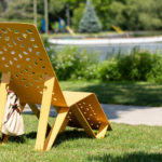 Yellow ALUM chaise lounge with bag attached facing water on grass