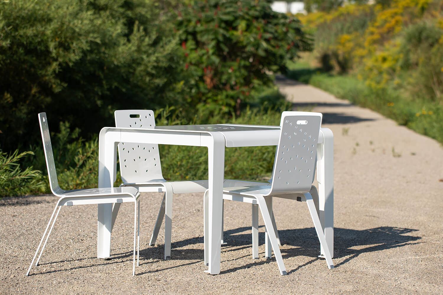 ALUM table and chairs painted gloss white sitting on gravel next to greenery