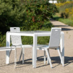 ALUM table and chairs painted gloss white sitting on gravel next to greenery