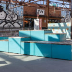 Turquoise painted Maglin Pixel Blocks are stacked on a patio with robot murale in background at Camp North End