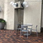 Foro Maglin tables and seating next to concrete wall with giant bulb lighting and planter