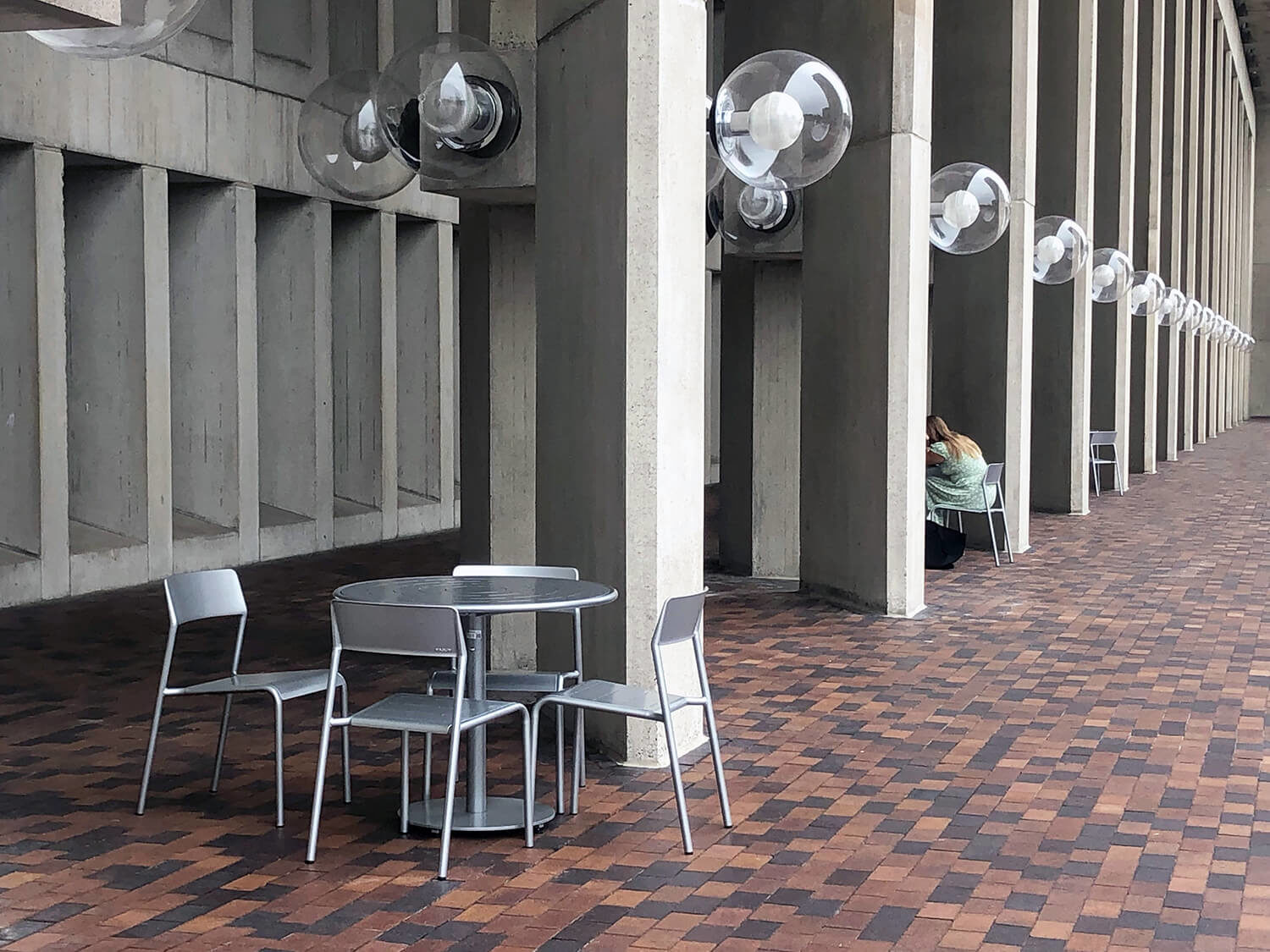 Foro tables and seating next to concrete pillars and interlocking brick