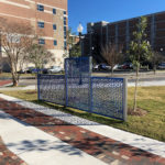 Blue and silver FLEXX panels line a walkway creating privacy from the road