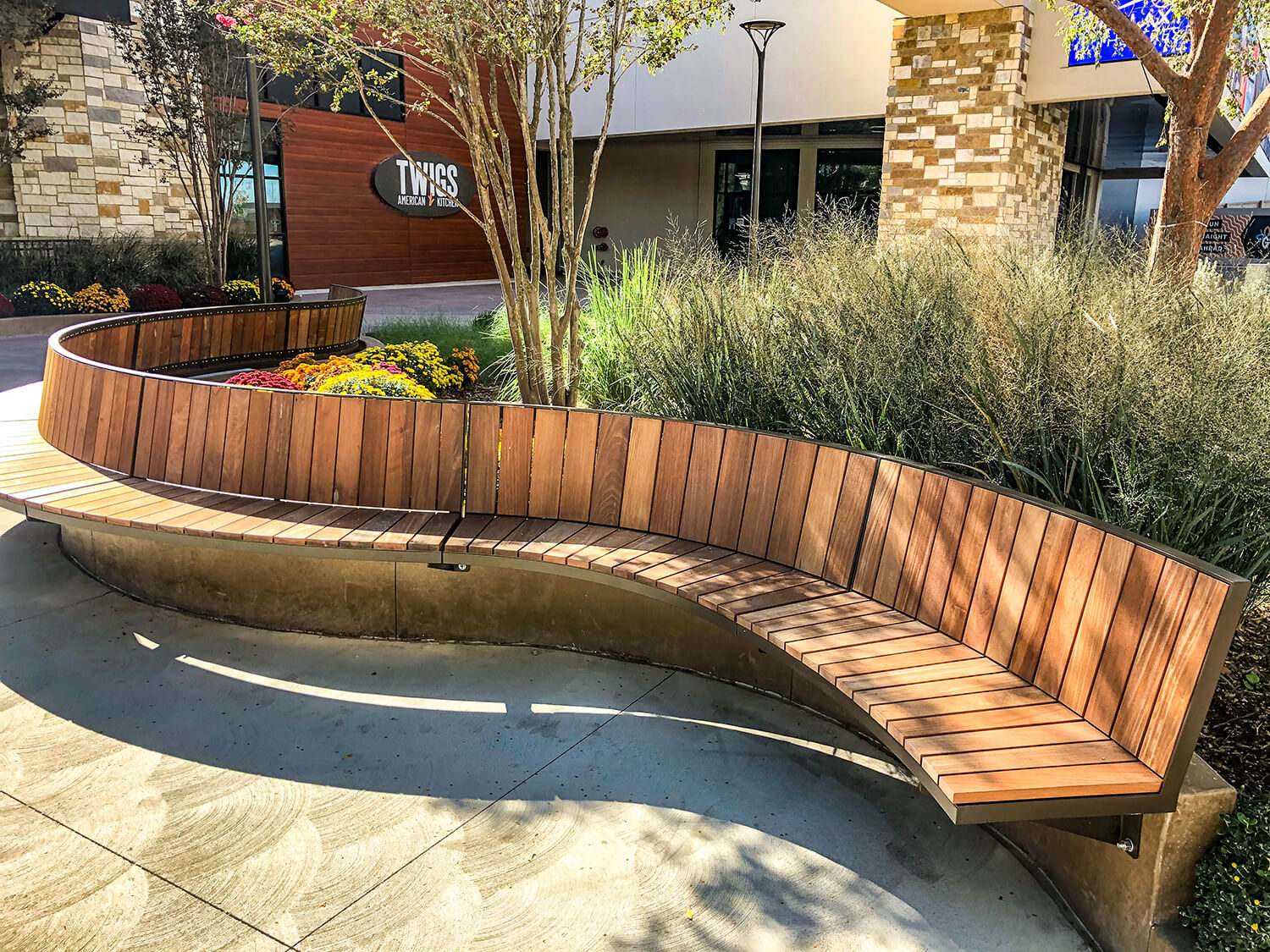 Curved Ogden bench cantilevered to a concrete ledge with gardens and buildings in background
