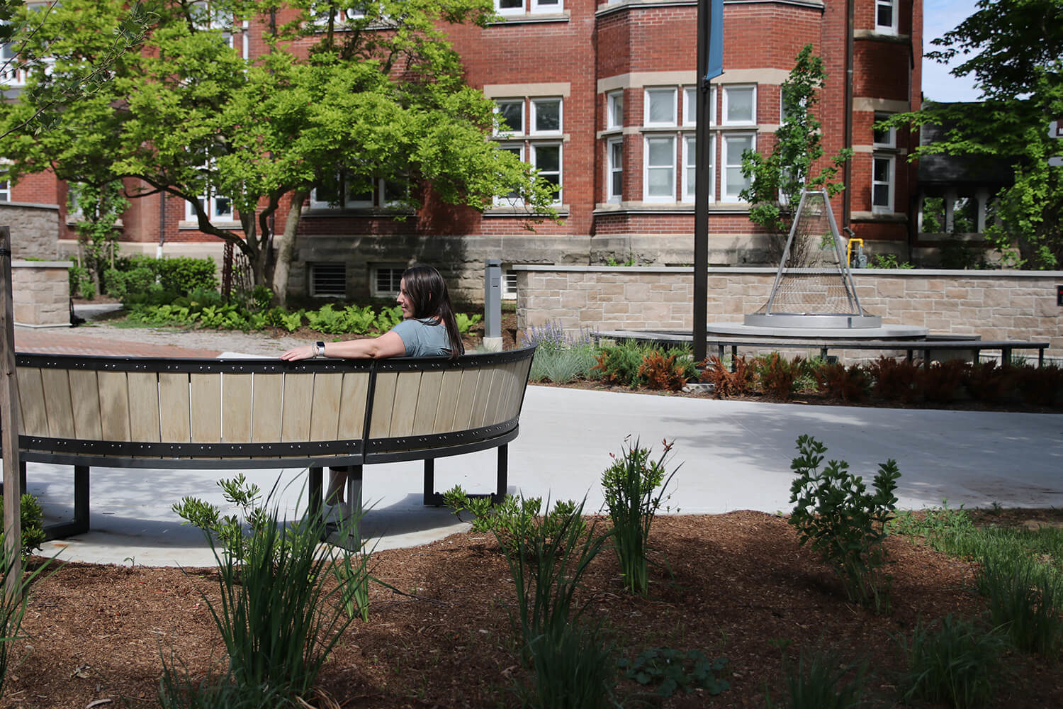 Student admiring the scenery while sitting on curved bench with red building in background and gardens
