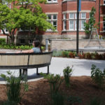 Student admiring the scenery while sitting on curved bench with red building in background and gardens