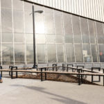 Mitered Ogden benches form a triangle in from of complex with people walking