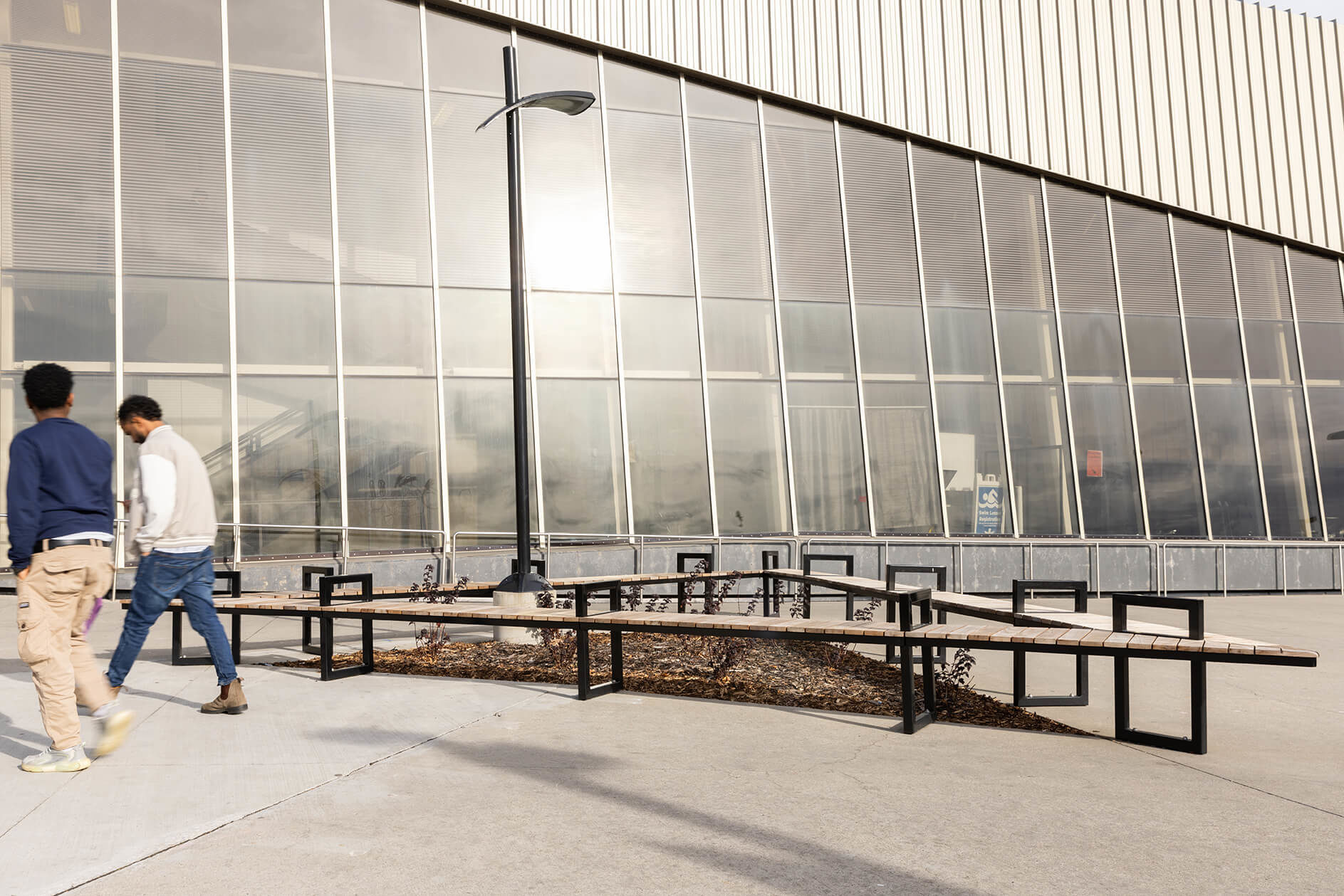 Mitered Ogden benches form a triangle in from of complex with people walking