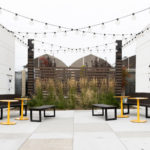 Maglin Ogden backed and backless benches with Ogden tables on outdoor patio with string lights