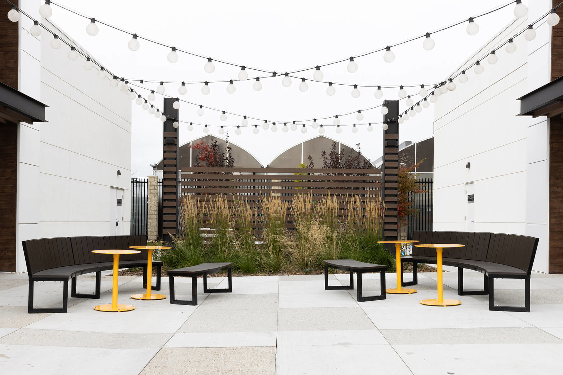 Maglin Ogden backed and backless benches with Ogden tables on outdoor patio with string lights
