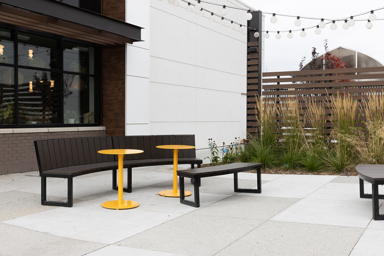 Yellow Ogden Cafe tables paired with Backed and Backless Ogden benches on outdoor patio with hanging lights