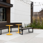 Yellow Ogden Cafe tables paired with Backed and Backless Ogden benches on outdoor patio with hanging lights