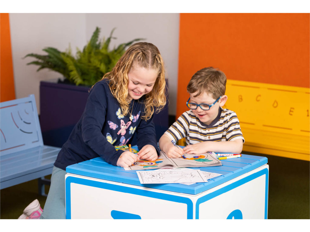 Children coloring books on pixel block with blue and yellow benches in background