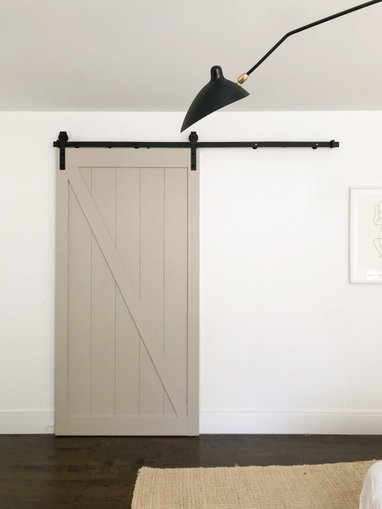 Beige sliding barn door with black hardware on a white door.