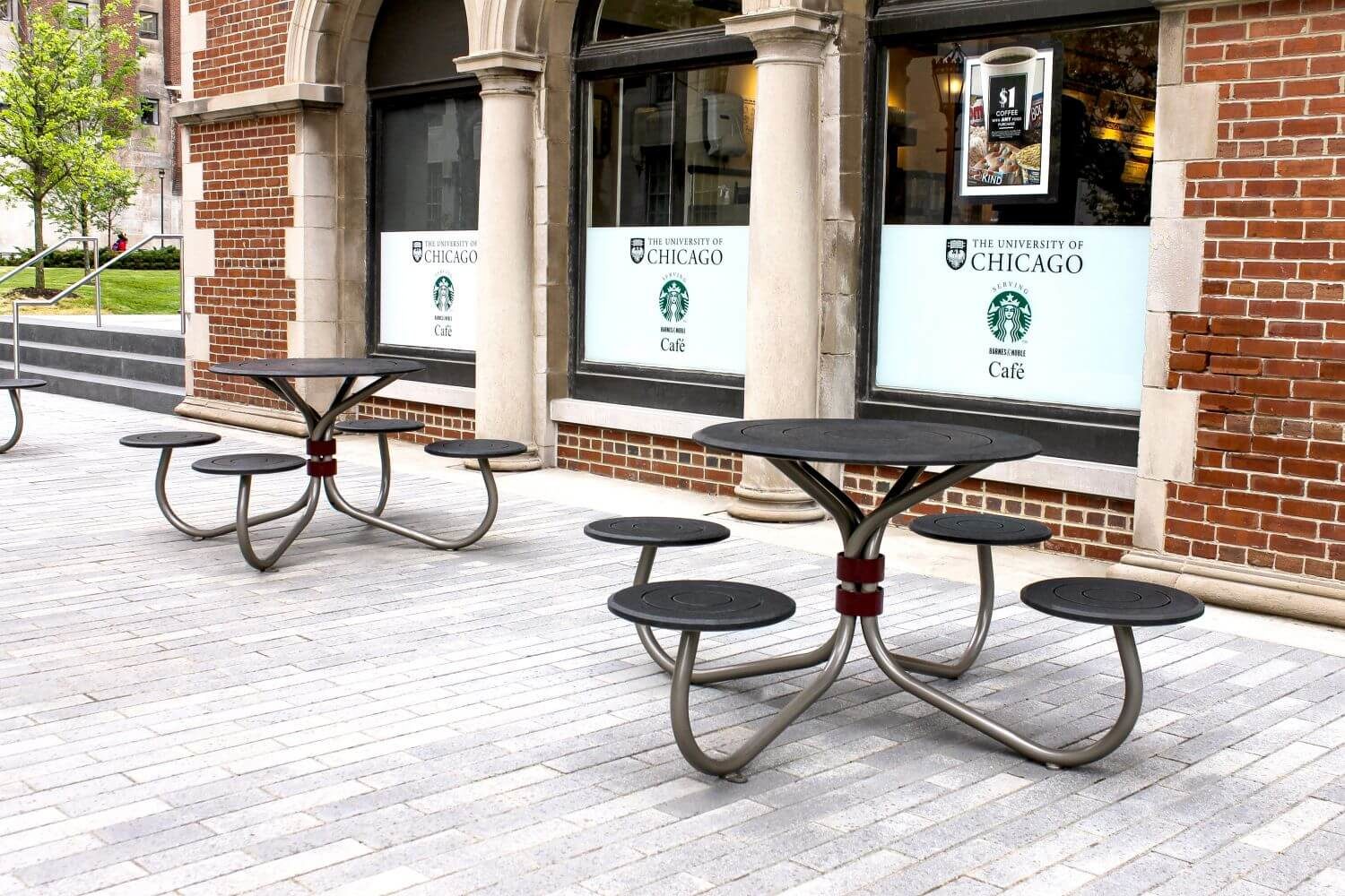 Black tables with four round seats outside red brick building