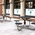 Black tables with four round seats outside red brick building