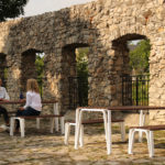 Two Women sitting at Table and Backless Benches Near a Stone Wall
