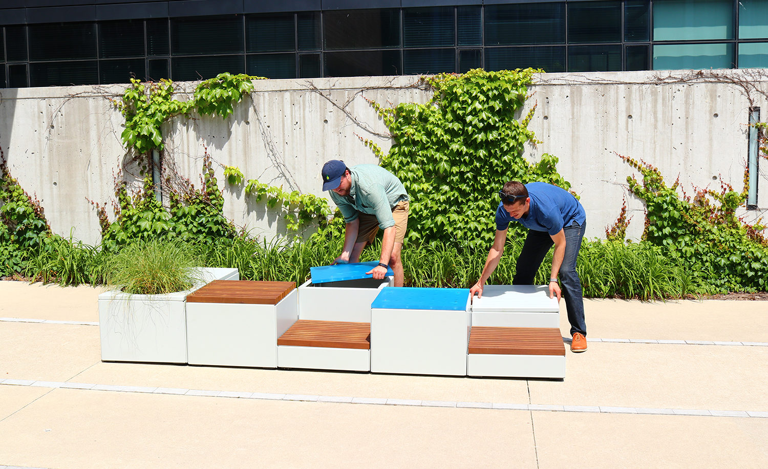 Two men assembling Pixel blocks against a wall with greenery