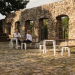 Iconic tables and seating with people in background against stone wall