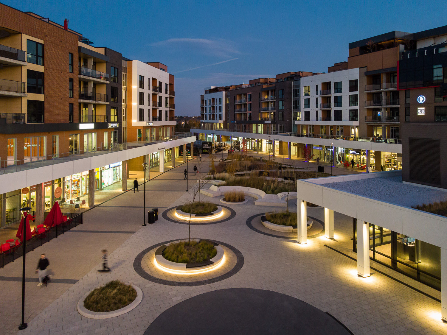 A nighttime top view of the lighting in AGORA Plaza, featuring Ogden Wall-mount benches and several Maglin 650 Waste and Recycling Containers.