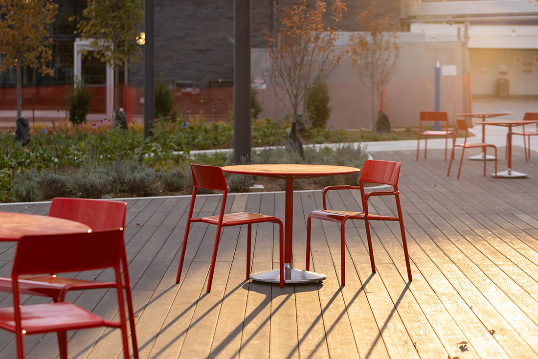 A set of red FORO chairs and Battery Tables are on the deck of Bathurst Quay Common in the late afternoon sun.