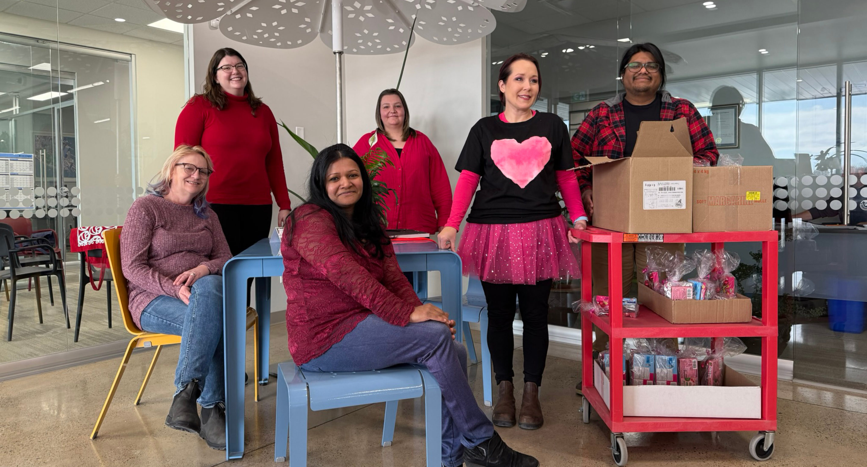 Maglin employees pose for a photo on Valentine's Day! Sarah wears a black t-shirt with a pink heart and Edgar has a tray of Valentine's Day goodies.
