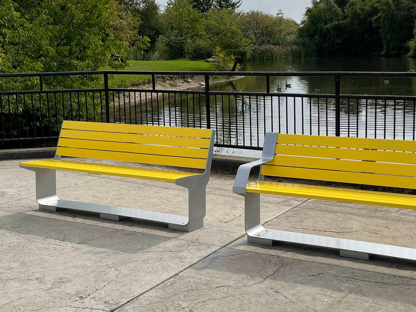 Brightly painted L-Series Backed Benches in front of pond and railing