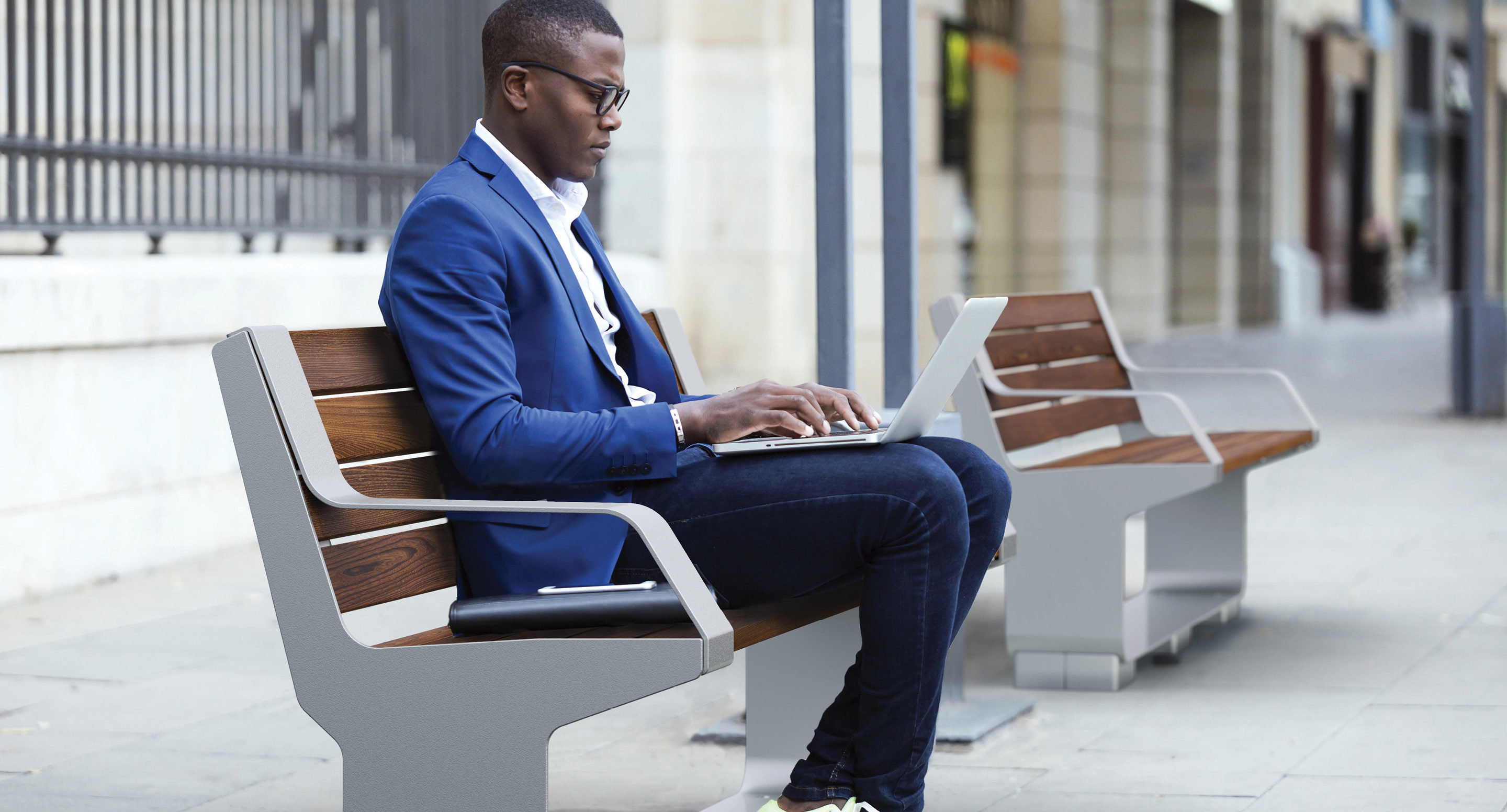 Man in blue coat sitting on bench while using laptop