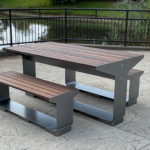L-Series table with backless benches in wood on patio next to pond and fence