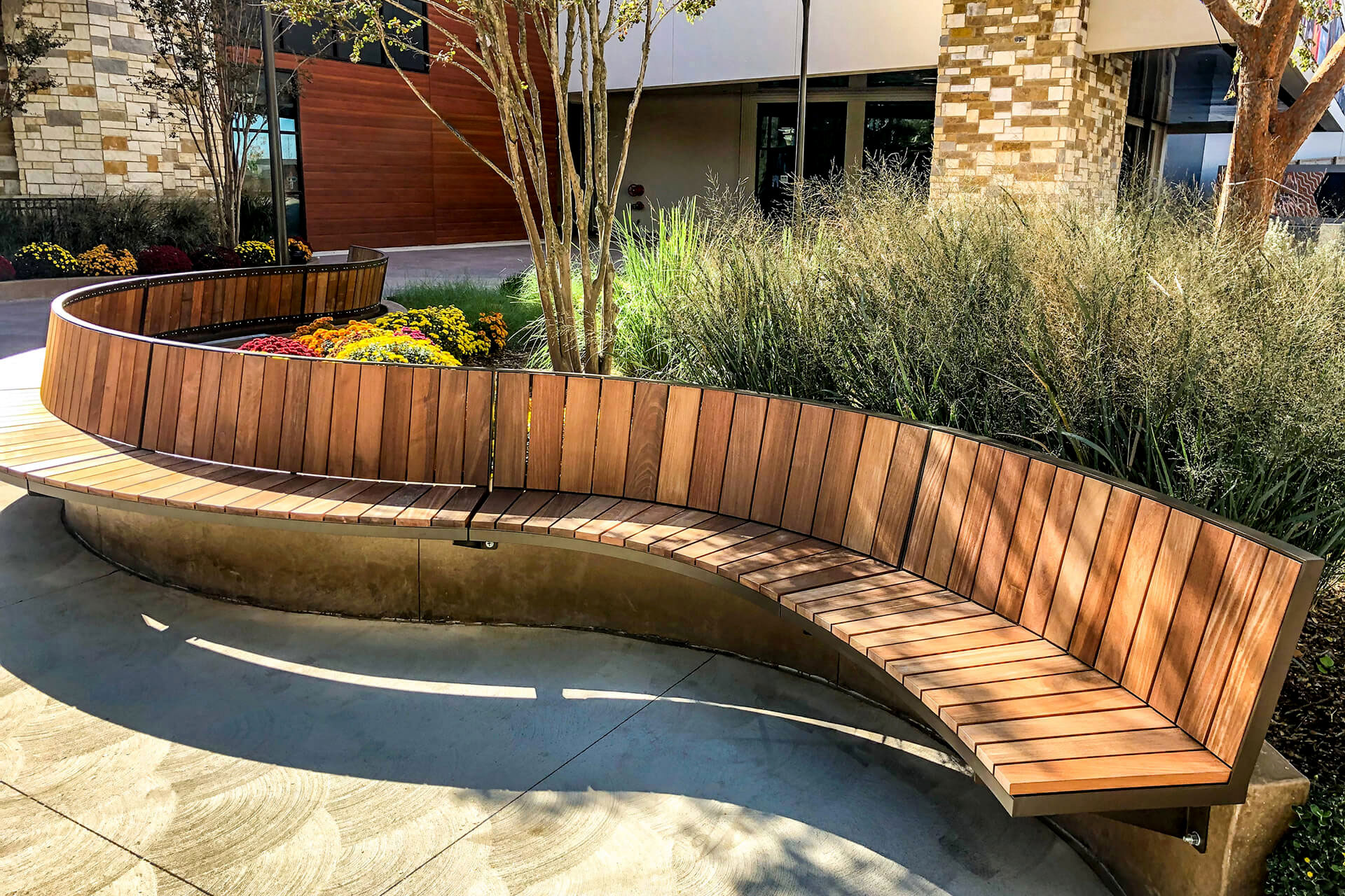 Ogden curved cantilever mount bench with green grasses and building