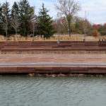 Lake Forest custom amphitheatre made of wood set on a pond with trees and shrubs in background.