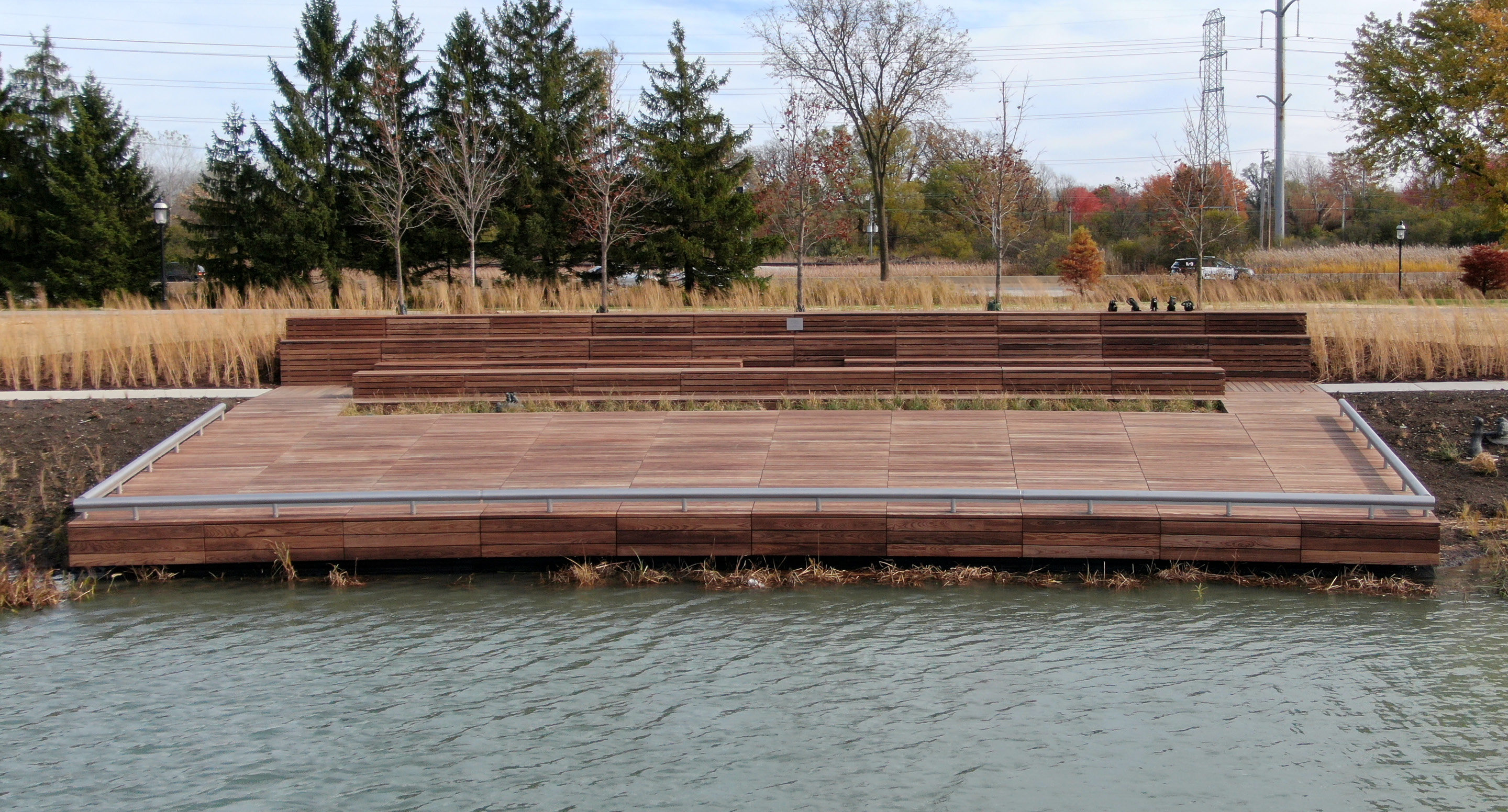 maglin-products_custom-hero Lake Forest custom amphitheatre made of wood set on a pond with trees and shrubs in background.